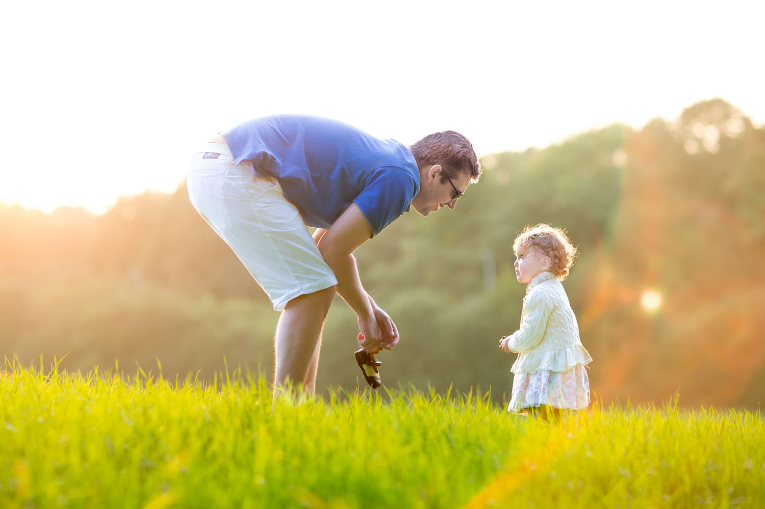 Young father playing with his baby daughter in a field on a sunny autumn evening